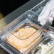 A gloved hand places a Cambro clear polycarbonate lid on a plastic container of food.
