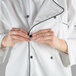 A person buttoning a white Mercer Culinary chef coat with black piping.
