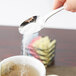 A hand using a Libbey stainless steel teaspoon to pour sugar into a cup of tea.