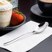 A Libbey stainless steel dessert spoon on a napkin next to a bowl of strawberries.