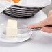 A hand using a Reserve by Libbey stainless steel bread and butter knife to slice butter on a plate.