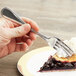 A hand holding a Libbey stainless steel dessert fork over a piece of pie.