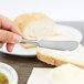 A person holding a Libbey stainless steel butter spreader over a piece of bread.