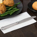 A stainless steel Libbey dinner knife on a white napkin next to a plate of food.