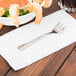 A Libbey stainless steel cocktail fork on a napkin next to a bowl of shrimp.
