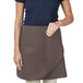A woman wearing an Intedge brown poly-cotton waist apron.
