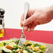 A hand holding a Libbey stainless steel dinner fork over a salad.