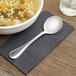 A Libbey stainless steel round soup spoon sits on a napkin next to a bowl of soup.