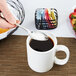 A hand using a Libbey stainless steel teaspoon to stir sugar into a mug of coffee.