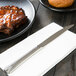 A World Tableware Varese steak knife on a napkin next to a plate of meat.