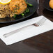 A World Tableware Varese salad fork on a napkin next to a plate of food.