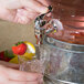 A hand using an Acopa silver spigot to pour water with a lemon and strawberry into a glass.