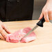 A hand using a Mercer Culinary semi-flexible narrow boning knife to cut meat on a cutting board.