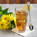 A glass of iced tea with a Libbey stainless steel iced tea spoon, ice, and lemon slices on a white background.