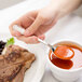 A hand holding a Libbey stainless steel bouillon spoon over a bowl of red soup.