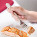 A person holding a Libbey Geneva stainless steel fish fork over a piece of food.