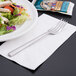 A Libbey stainless steel salad fork on a plate of salad with a packet of condiments.