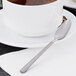 A cup of coffee with a Libbey Cimarron stainless steel demitasse spoon on a plate.