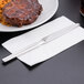 A Libbey stainless steel dinner knife on a white napkin next to a plate of steak and rice.