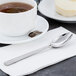 A cup of tea on a plate with a Libbey stainless steel teaspoon on a napkin.