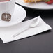 A stainless steel Libbey demitasse spoon on a napkin next to a cup of tea.