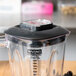 A Waring blender with a black lid on the counter in a smoothie shop.