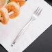 A World Tableware stainless steel cocktail fork on a napkin with shrimp.