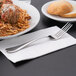 A Reserve by Libbey stainless steel dinner fork on a napkin next to a plate of spaghetti and meatballs.