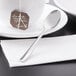 A Libbey stainless steel demitasse spoon on a white plate with a brown paper tag tied to a white tea cup.