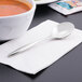 A Libbey stainless steel bouillon spoon on a napkin next to a bowl of soup.