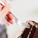 A person holding a Libbey stainless steel dessert fork over a piece of chocolate cake.
