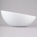 A Tablecraft white melamine bowl with a curved edge on a gray surface.