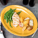 A Libbey saffron oval porcelain platter with chicken, potatoes, and green beans.