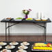 A black rectangular plastic tablecloth with elastic on a table with plates of food.