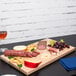A Vollrath hardwood display cutting board with meats and cheese on it on a table.