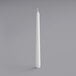 A Will & Baumer white taper candle on a gray surface.