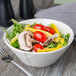 A Libbey Farmhouse ivory serving bowl filled with salad with tomatoes and mushrooms.