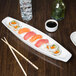 A Libbey ultra bright white porcelain canoe tray with sushi and chopsticks on it.