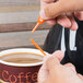 A person using a Royal Paper Stix To Go orange beverage plug and stirrer to stir a cup of coffee.