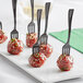 A close up of Visions black plastic tasting forks on meatballs.
