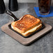 A grilled cheese sandwich on a Lodge square wood underliner with a drink on a table.