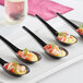 A white plate with four Visions black plastic Asian soup spoons filled with food.