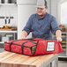 A man in a chef's hat holding a red ServIt insulated pizza bag with pizza boxes inside.