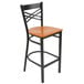 A Lancaster Table & Seating black metal cross back bar stool with a cherry wood seat.