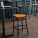 A Lancaster Table & Seating black cross back bar stool with a cherry wood seat on a table in a restaurant.