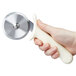 A hand holding a Dexter-Russell pizza cutter with a white handle.