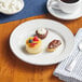 An Acopa Bright White stoneware plate with a chocolate covered pastry and a cup of coffee on a table.