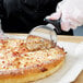 A person using a Dexter-Russell pizza cutter to cut a slice of cheese pizza.
