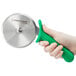 A hand with a green plastic handle using a Dexter-Russell pizza cutter.