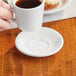 A person holding a cup of coffee on a Acopa bright white saucer.